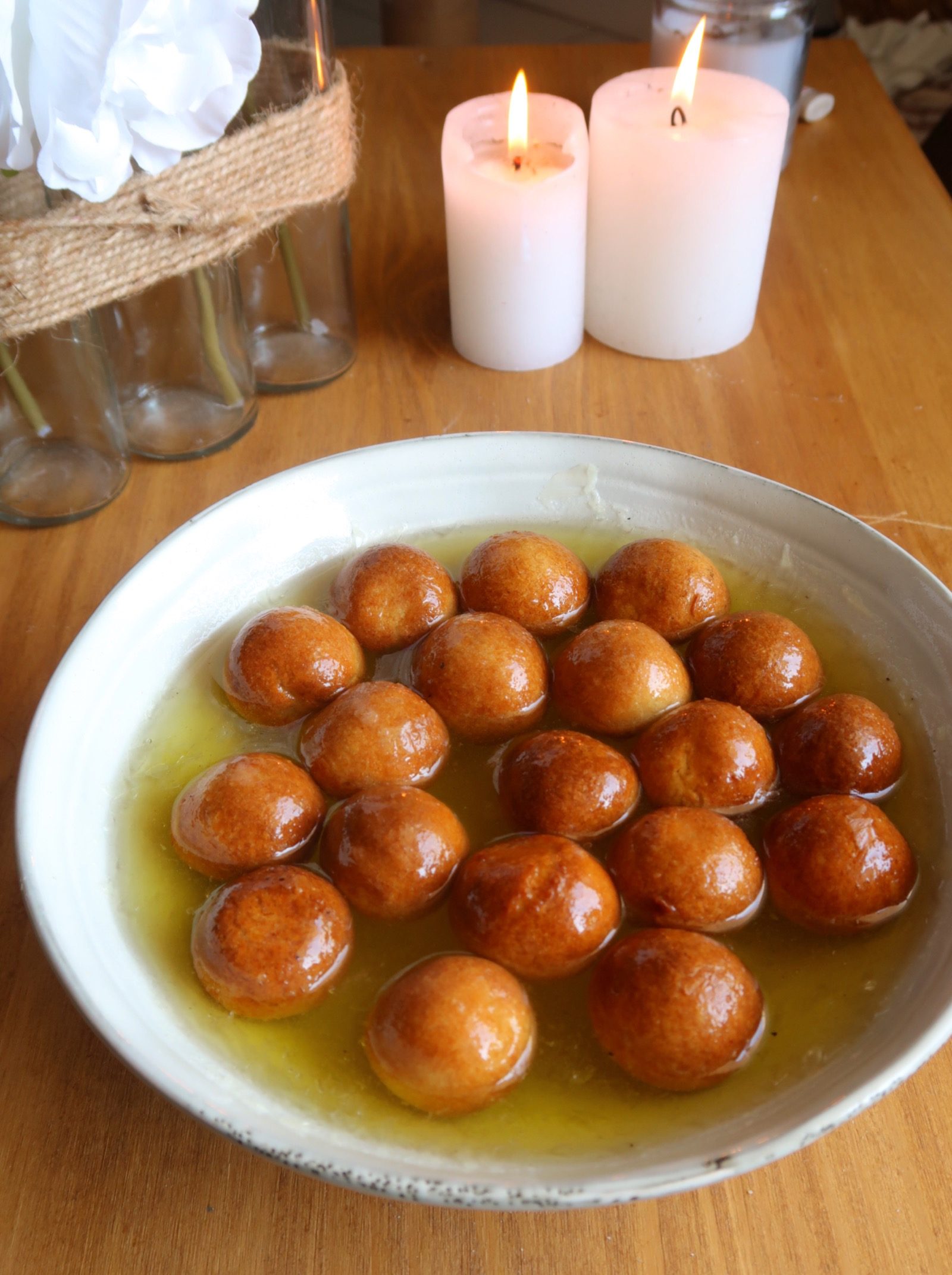 Vegan Gulab Jamun served in a bowl surrounded by 2 candles