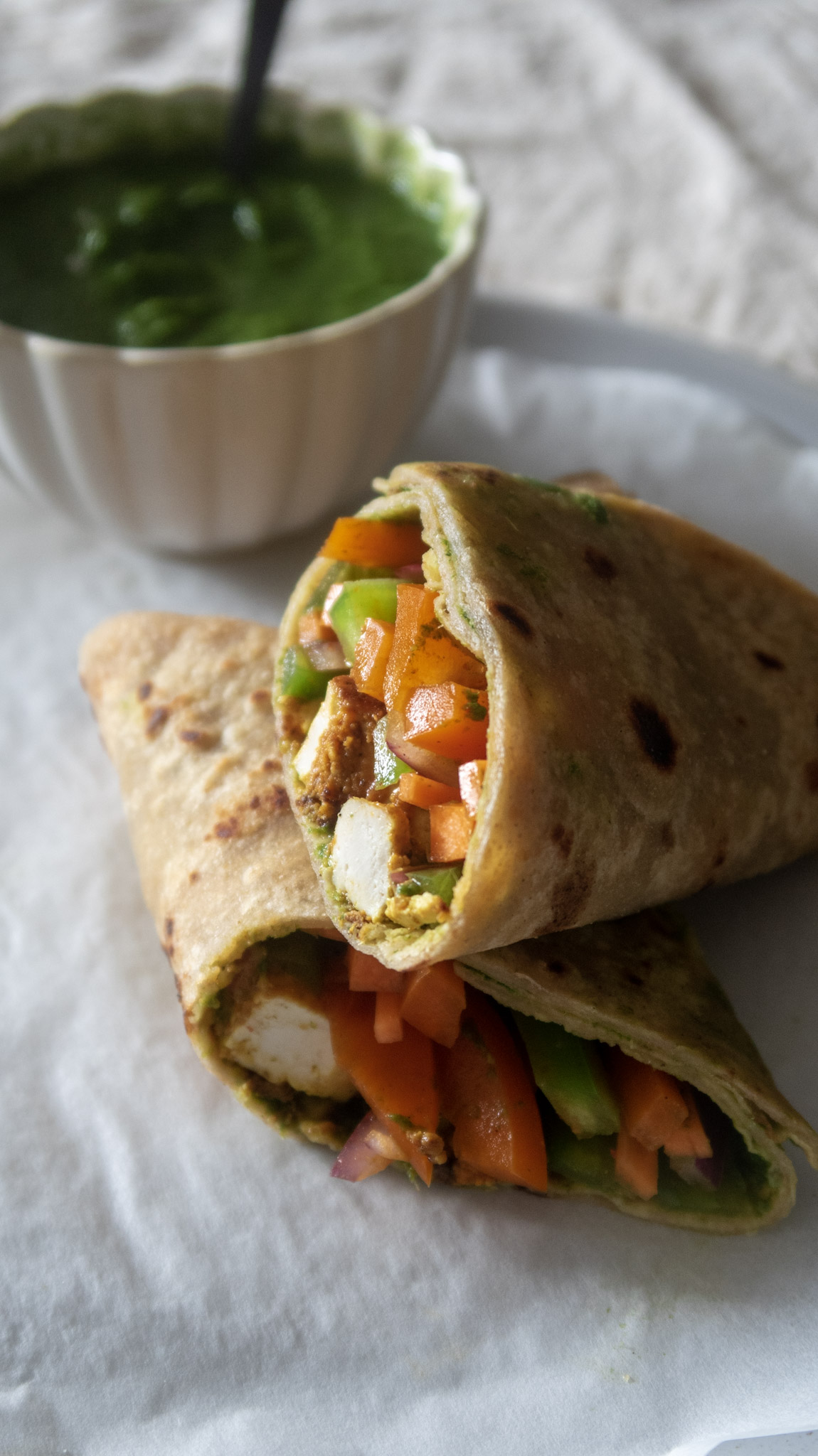 Vegan Kathi rolls cut in half an served on a plate with mint coriander chutney on the side in a mini bowl