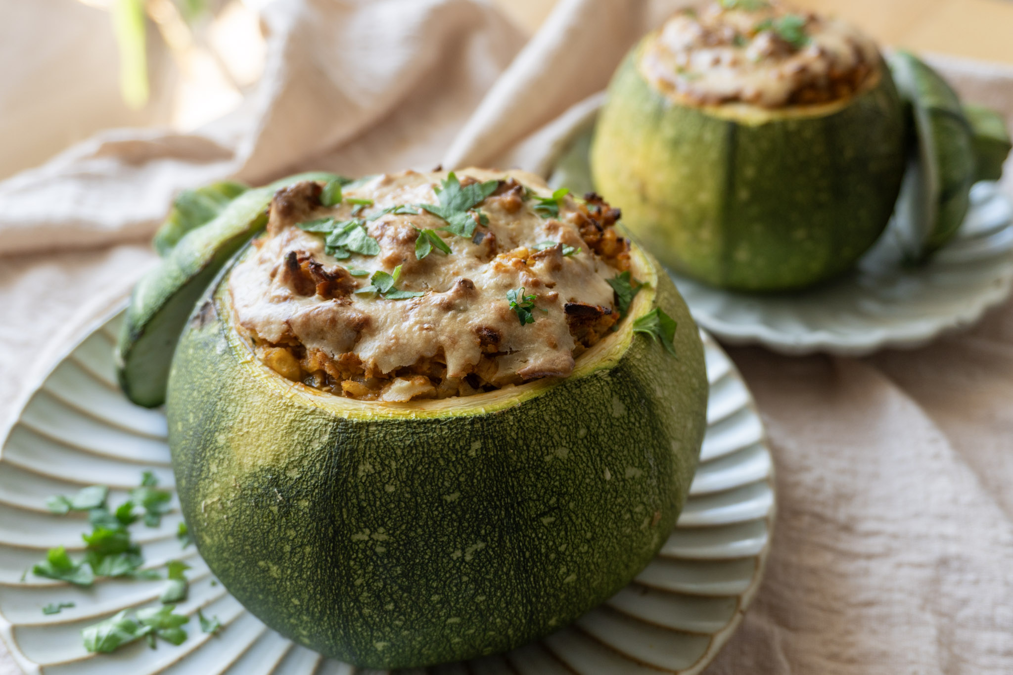 Baked stuffed round zucchni served on a plate with corrainder and cashew cream garnish