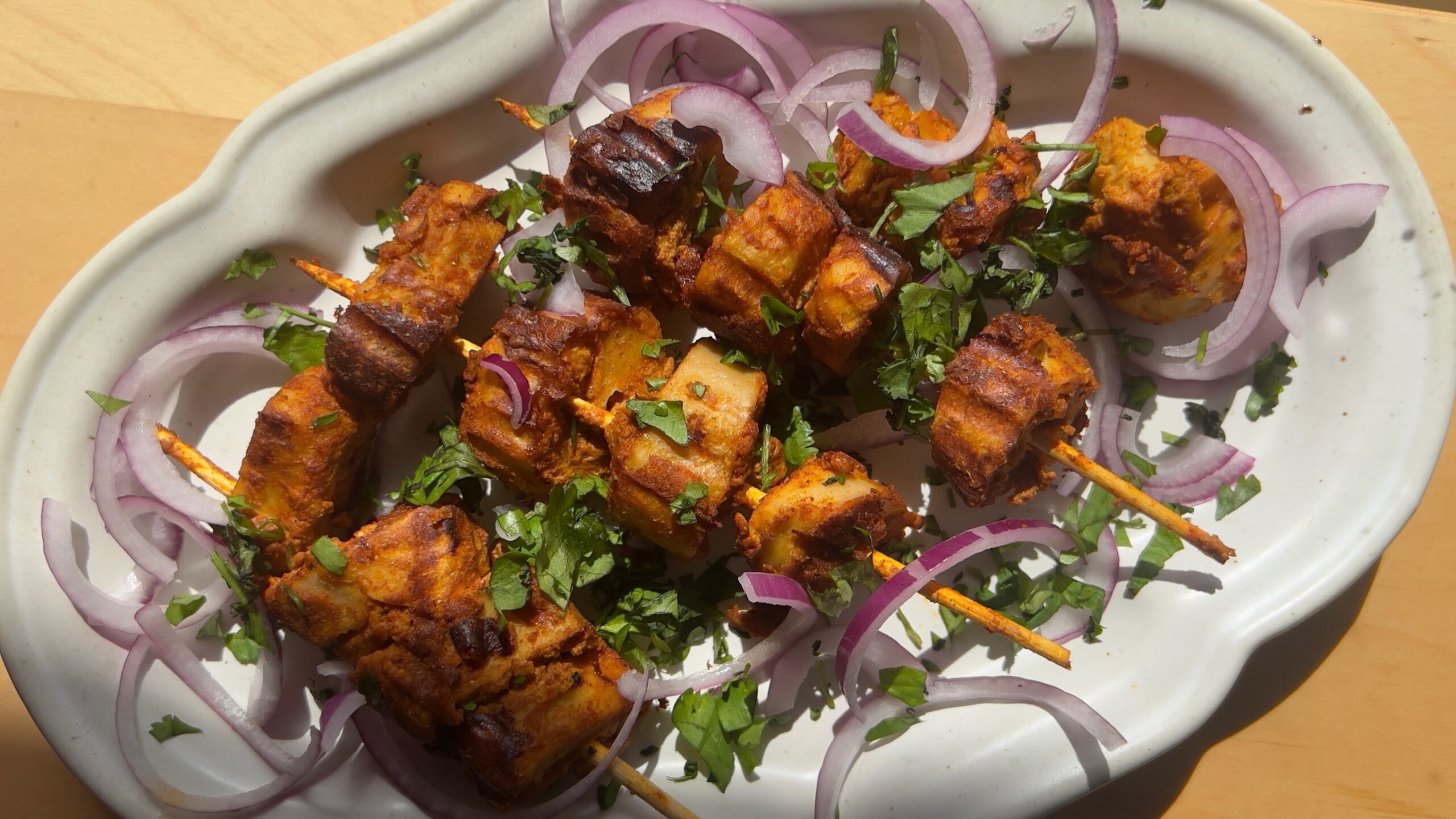 Grilled tandoori soya chaap arranged on a plate garnished with corriander and onions