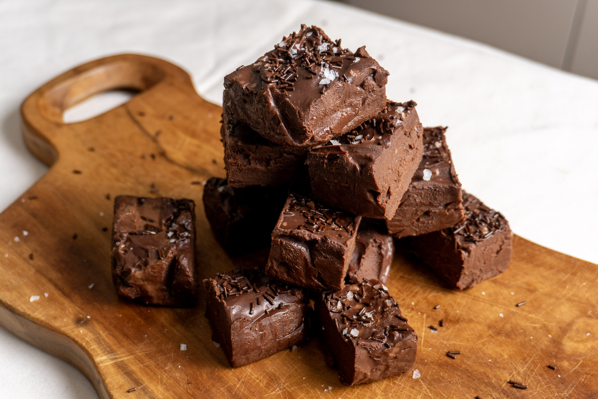A pyramid of fudge pieces on a wooden chopping board, with one piece taken a bite out off. Bird's eye shot.