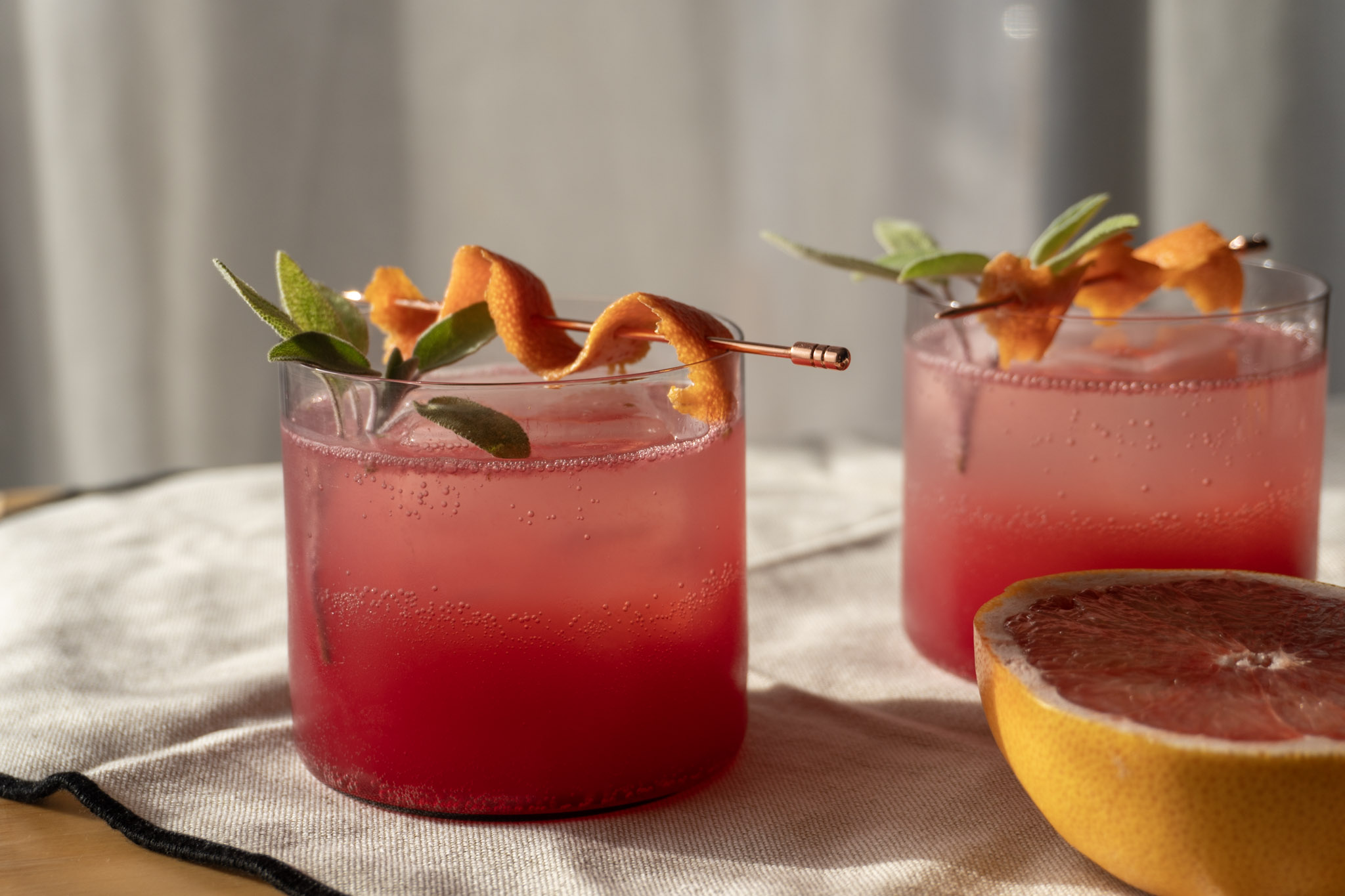 Two glasses of Grapefruit Sage Bitters Mocktail, garnished and served, showcasing the vibrant color and elegant presentation of the drink. Front view