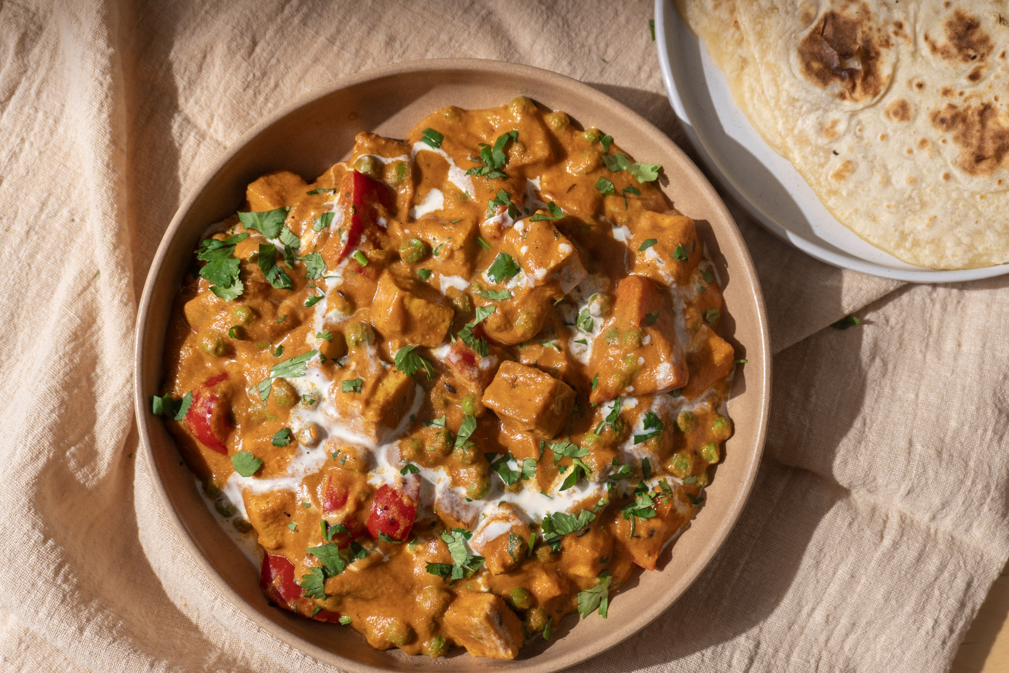 Vegan Matar paneer served in shallow bowl with naan on the side. Top view.