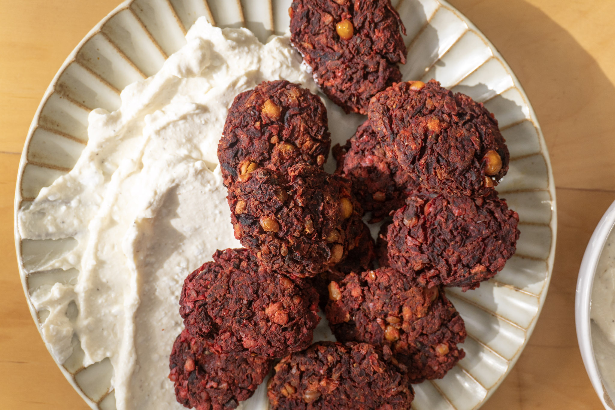 Beetroot chickpea fritters on a plate with whipped feta dip, top view.