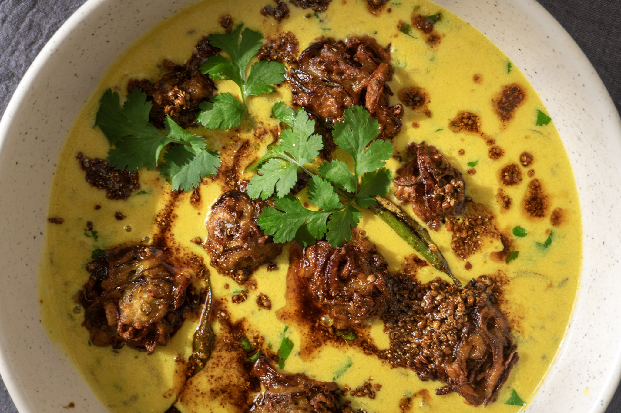 Top shot: Vegan Punjabi Kadhi served in a bowl garnished with tempering, coriander and onion fritters