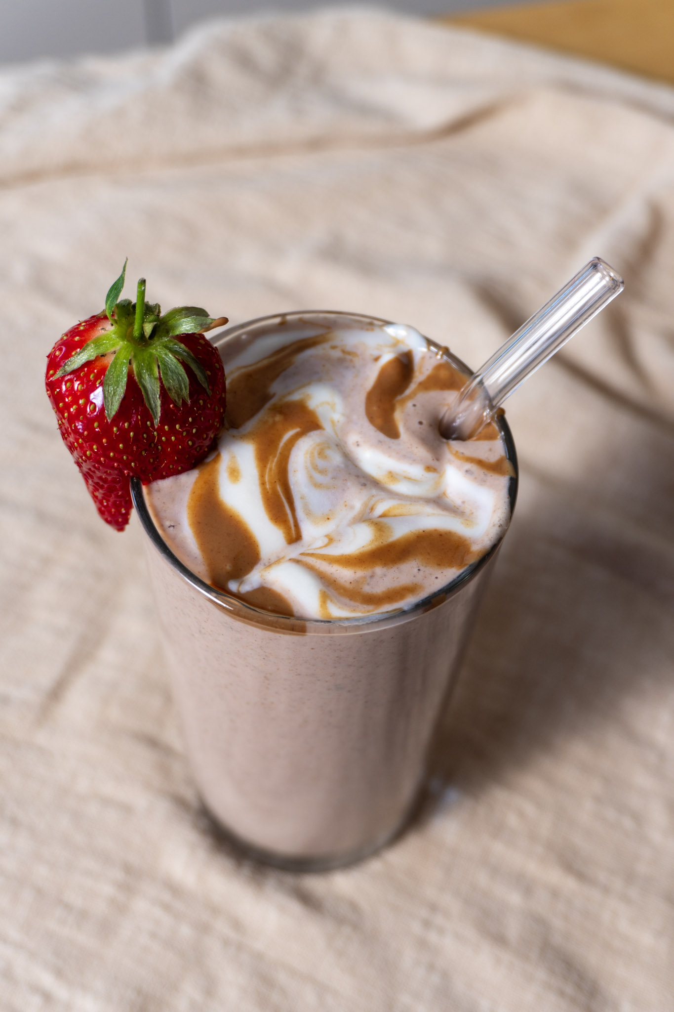 Date Strawberry Protein Smoothie in a tall glass garnished with a fresh strawberry and a clear straw