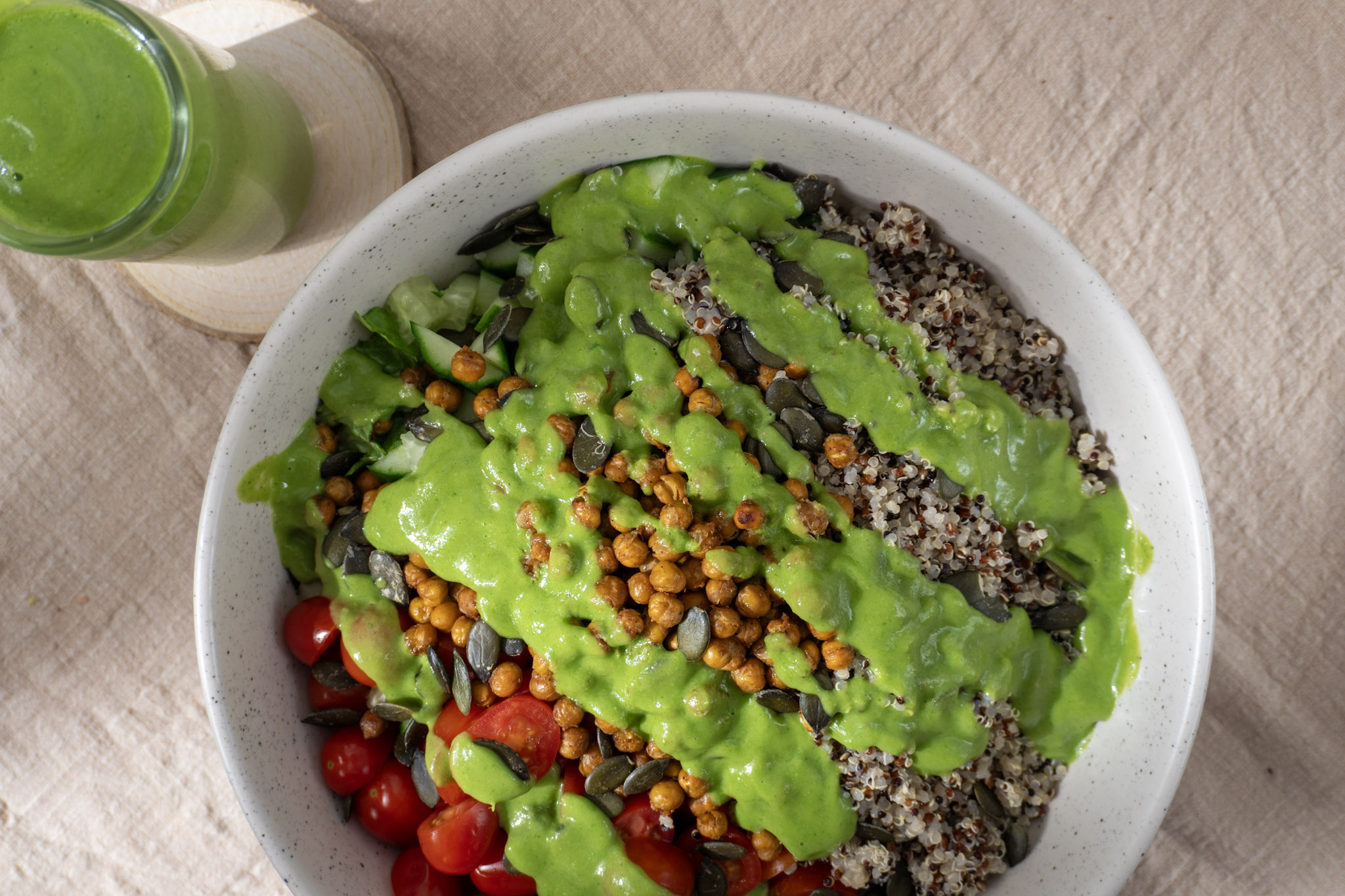 A vibrant, healthy salad bowl featuring a mix of quinoa, cherry tomatoes, crispy chickpeas, and pumpkin seeds, all generously drizzled with a bright green chutney salad dressing. Top view.