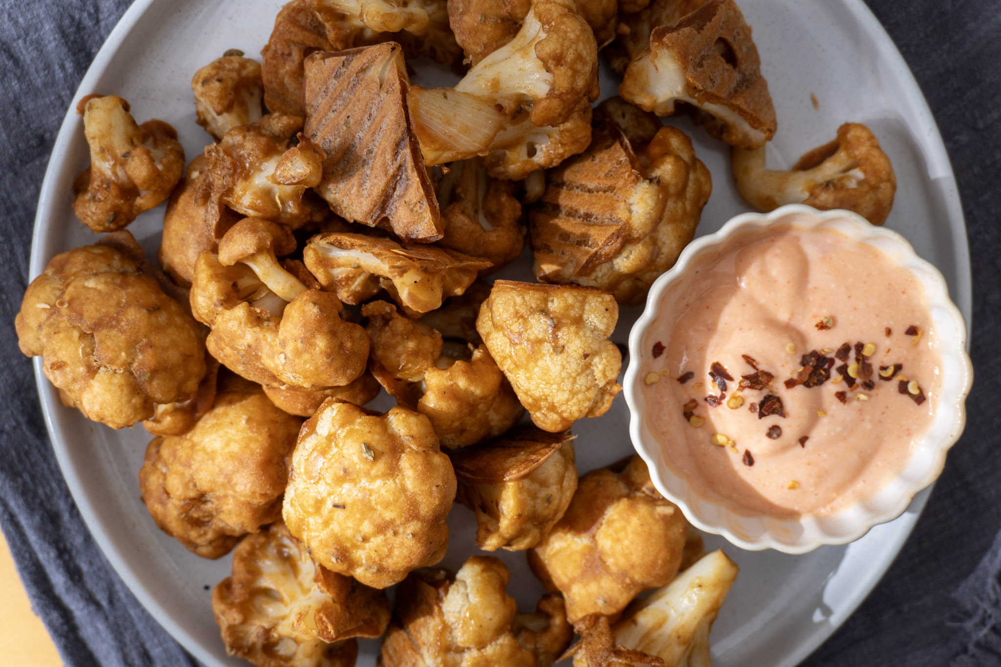 Easy baked cauliflower wings served on a white plate with a dip on the side. Top view.