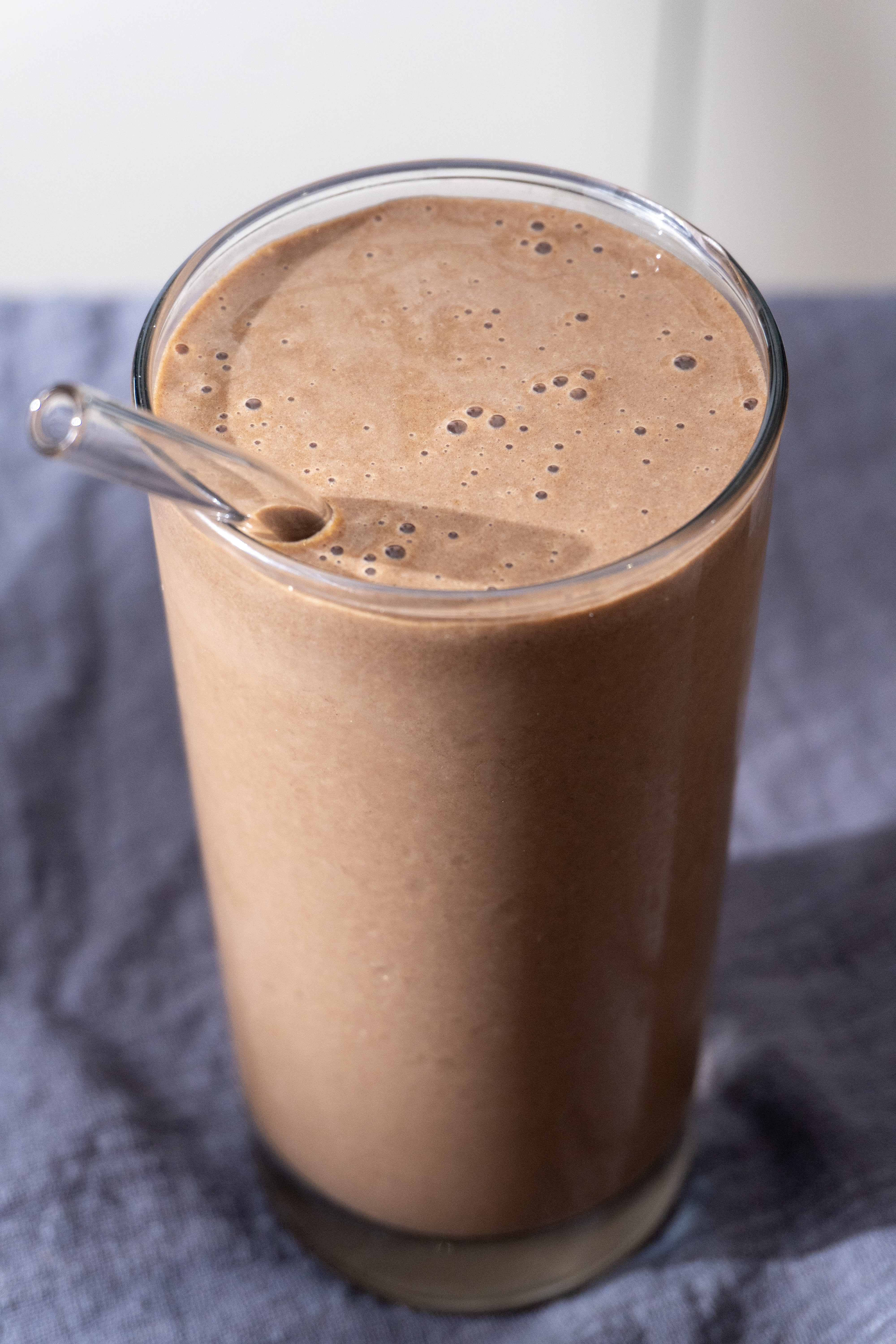 Chocolate cauliflower protein smoothie in a tall glass with a straw