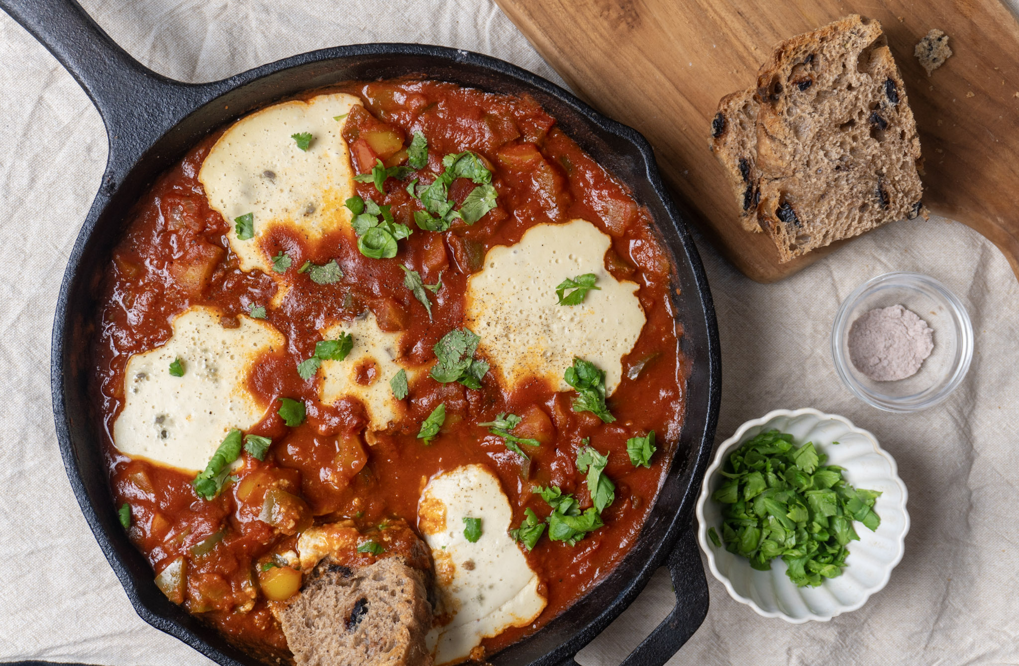 birds eye view of vegan shakshuka in cast iron skillet garnished with cilantro with sourdough bread loaf and extra cilantro garnish on the side