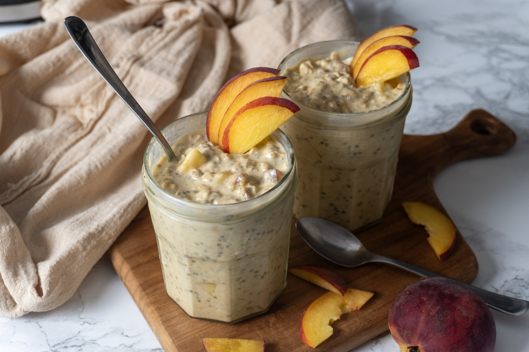 two cups of overnight oats side by side garnished with peach slices and a spoon in one of them