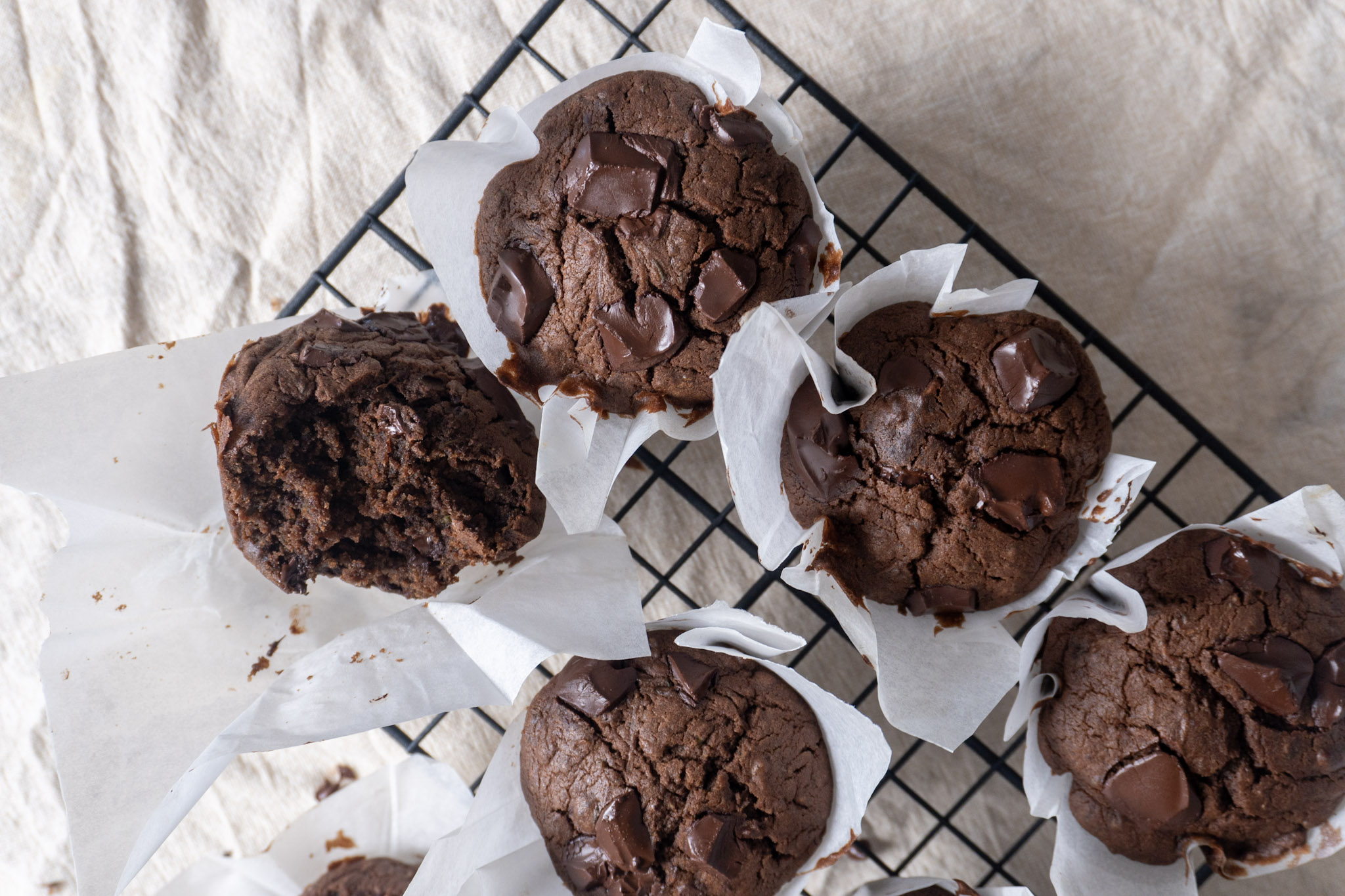 fudgy chocolate zucchini muffins on a wire rack, with one muffin taken a bite out of
