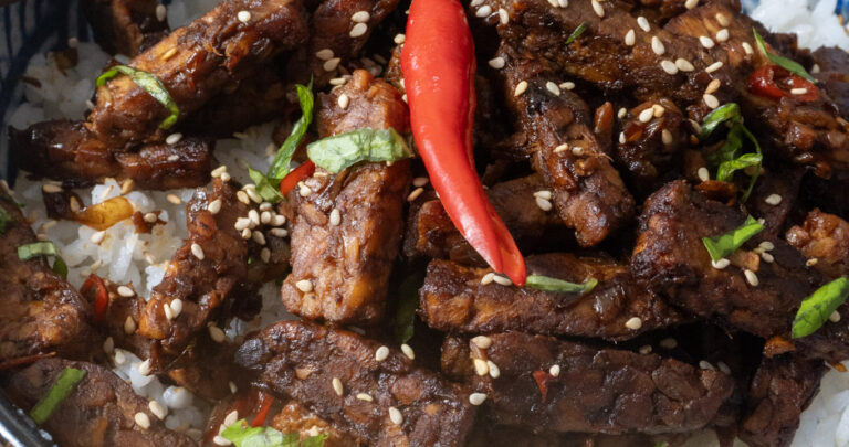 top view of bowl of Indonesian tempeh stir-fry garnished with a red chili with chopsticks on top
